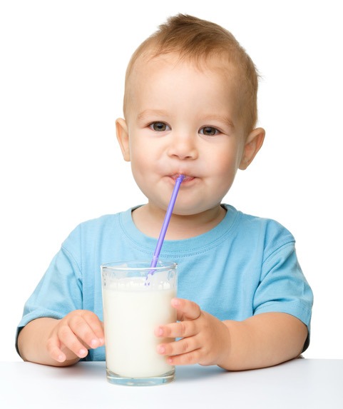 Cute little boy is drinking milk using straw while sitting at table