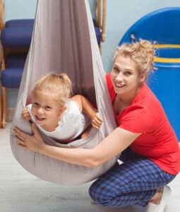 Therapist working with child hanging in a swinging pod