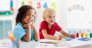 Two Preschool Age Children Smiling at a Desk working on a project