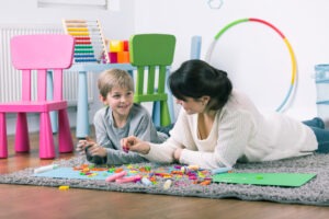 Therapist and little boy having fun together playing with letters and chalk