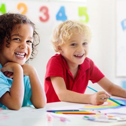 Two Preschool Age Children Smiling at a Desk working on a project