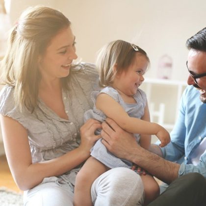 Parents sitting on floor with toddler smiling