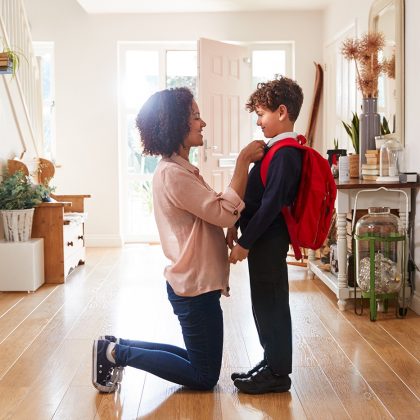 Mom kneeling at eye level with child wearing backpack