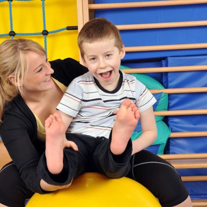 Woman As A Therapist At Physiotherapy With Medicine Ball With Child In Gym